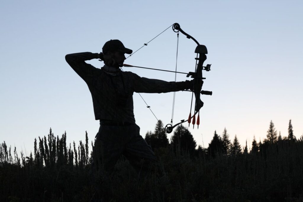 Person mit Compoundbogen in der Natur bei Sonnenuntergang, konzentriert im Schussmoment