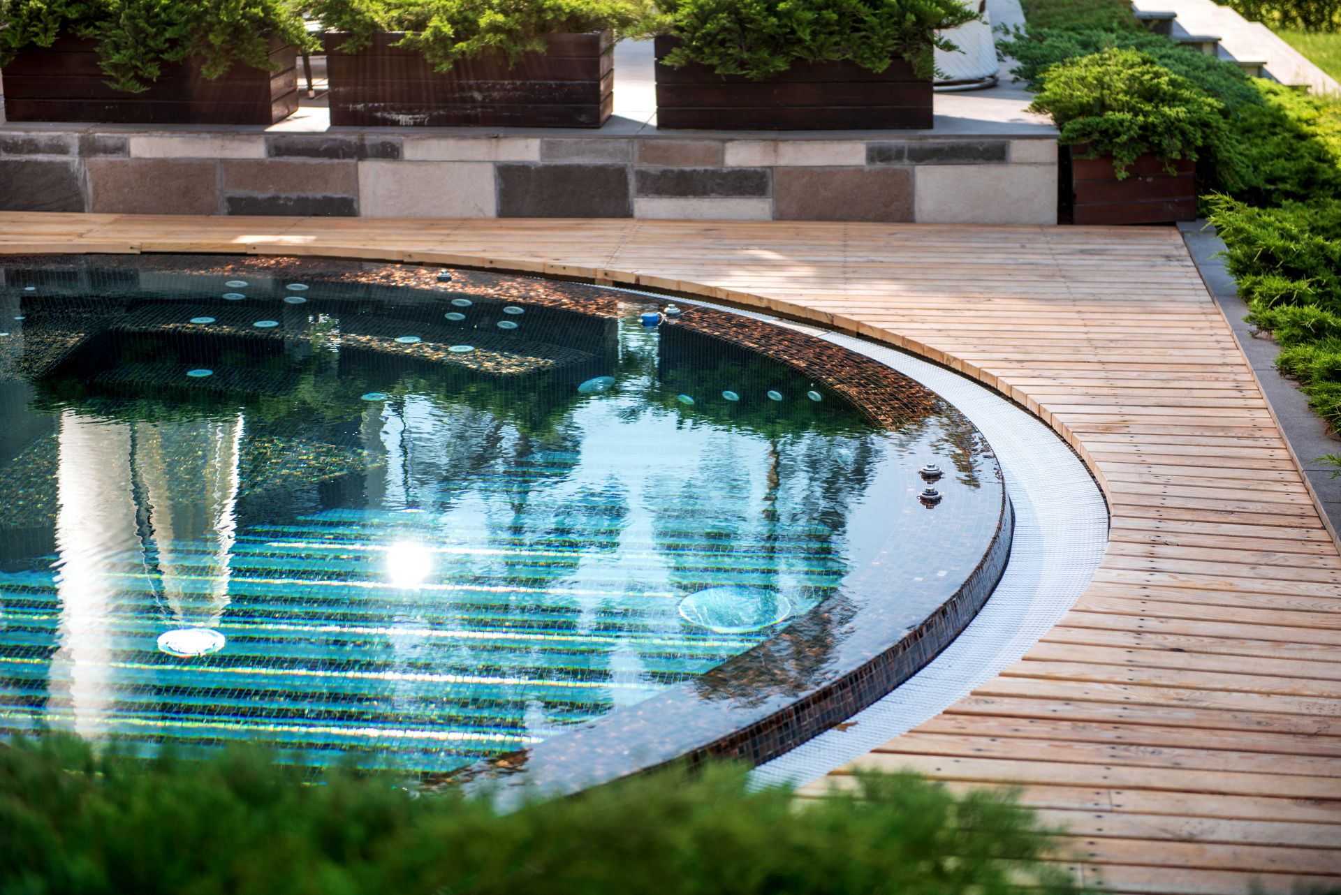 Modern gestalteter runder Pool mit Holzdeck und Pflanzenumrandung im Garten
