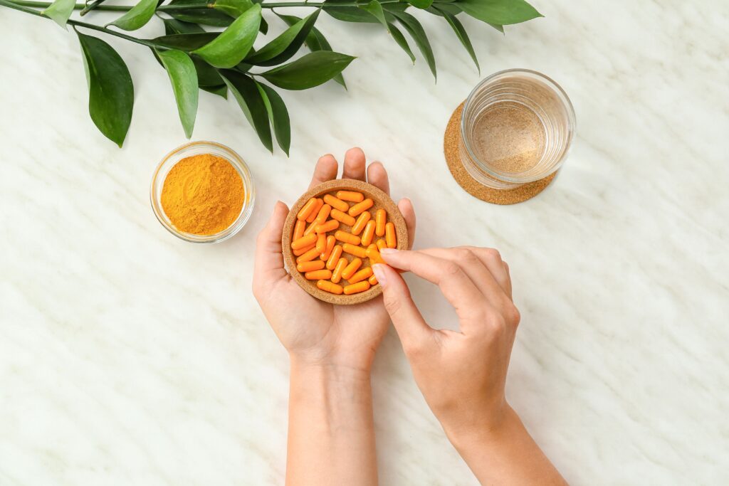Curcuma Kapseln in Hand mit Kurkumapulver und Glas Wasser auf hellem Hintergrund
